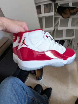 Air Jordan 11 Cherry röda och vita - Säljer ett par Air Jordan 11 Cherry sneakers i vitt och rött. Skorna har en blank röd lackdetalj runt hela skon, vit mesh på ovandelen och klassisk Jumpman-logga på sidan. Tjock vit sula med isblått genomskinligt parti. Perfekta för dig som vill sticka ut. Oanvända, om inte möjligtvis använda en gång.