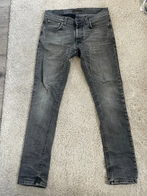 Grå slim fit jeans med slitningar - Säljer ett par grå slim fit jeans med snygga slitningar och tvättade detaljer. Jeansen har fem fickor och klassisk knappgylf. Bakfickorna har broderade detaljer. Perfekta för dig som gillar en avslappnad men trendig stil. Storleken är 30/32