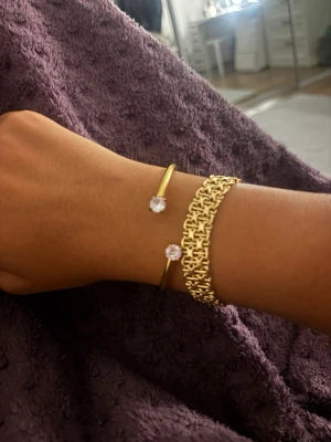 Guldarmband med stenar - (Inte X LÄNKEN!!) Snyggt guldarmband med två gnistrande stenar i ändarna. Armbandet har en öppen design och passar perfekt för att ge en lyxig touch till din stil. Kombineras enkelt med andra smycken för en trendig look.