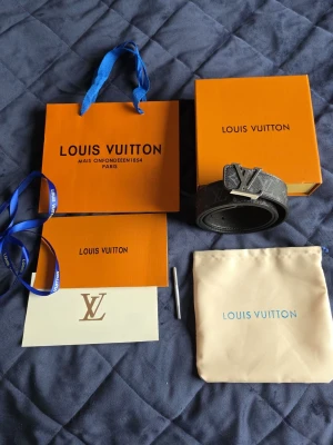 Louis Vuitton svart monogram skärp - Snyggt svart Louis Vuitton skärp med klassiskt monogrammönster och stor LV-logga i silver på spännet. Bältet har en exklusiv känsla och levereras med originalförpackning, dustbag och tillbehör. Perfekt accessoar för att lyfta din outfit.