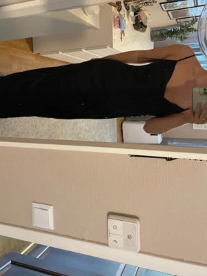Svart långklänning med slits - Säljer en elegant svart långklänning med smala axelband och slits på sidan. Klänningen har en figurnära passform och v-ringad urringning. Perfekt för dig som gillar stilrena och klassiska plagg.