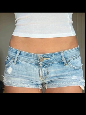 Lågmidjade jeansshorts från Hollister - Säljer ett par ljusblå lågmidjade jeansshorts från Hollister med slitna detaljer och fransig kant. Klassisk femficksmodell med knapp och dragkedja framtill samt snygga sömmar på bakfickorna. Perfekta för varma dagar! Fråga för mått! Första två bilderna är lånade då de ej passar mig!