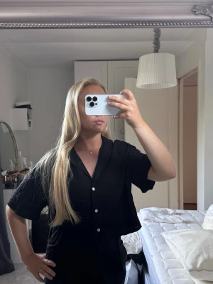 Svart kortärmad linne blus med knappar - Stilren svart linne blus med korta ärmar och klassisk krage. Blusen har en avslappnad passform och knäpps framtill med vita knappar. Perfekt till både jeans och kjol för en trendig look.