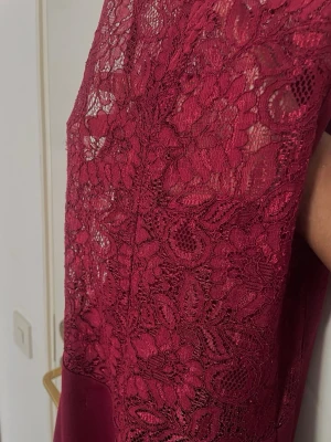 Vinröd spetsklänning i lång modell - Elegant vinröd långklänning med vackert spetsliv på ryggen och ärmlös design. Klänningen har en figurnära passform upptill och faller snyggt längs kroppen. Perfekt för speciella tillfällen när du vill sticka ut med stil. Haft i ett par år men endast använt en gång❤️Uppsydd sömm nedantill. Den sitter åt på mig och jag har storlek S så kan passa både S och XS.