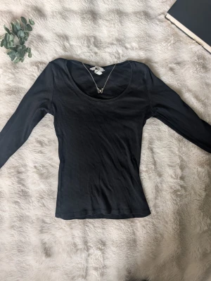 Svart långärmad topp med rund hals - En enkel och stilren svart långärmad topp med rund halsringning. Toppen har en tight passform och är tillverkad i ett mjukt och stretchigt material som känns skönt mot huden. Perfekt att matcha med jeans eller kjol för en clean look.