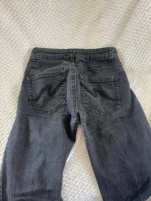 Svarta jeans med vågmönster bak - Säljer ett par svarta jeans med snyggt vågmönster på bakfickorna. Jeansen har klassisk femficksmodell, normal midja. Materialet är denim i bomull med en lätt tvättad look. Perfekta för dig som gillar en stilren men ändå unik detalj på jeansen.