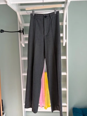 Gråa kostymbyxor med pressveck - Högmidjade kostymbyxor från pull & bear med raka ben och pressveck framtill. Använda väl men är tyvärr för små för mig numera. Inga tecken på slitage eller märken. Stl: XS men sitter som en XXS och passar nog någon mellan 157-162 cm lång
