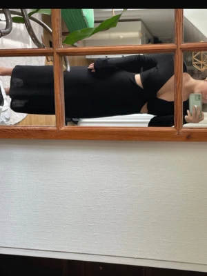 Svart långklänning med cut out - Snygg svart långklänning med långa ärmar och trendiga cut out-detaljer vid midjan. Klänningen har en kroppsnära passform och är perfekt för dig som vill sticka ut. Materialet ser ut att vara mjukt och stretchigt, vilket ger en bekväm känsla.