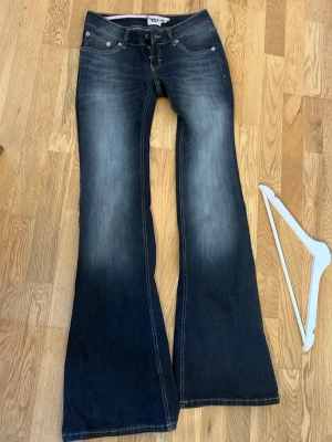 Mörkblå bootcut jeans från 157 - Snygga mörkblå bootcut jeans från 157 med slitningar framtill och kontrastsömmar. Klassisk femficksmodell och låg midja. Perfekta för dig som gillar en retro och avslappnad stil. Materialet är denim i bomull. Jag satte skosnöre i midjan men de får ta bort utan att de syns på utsidan