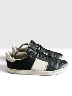 Valentino garavani flycrew sneckers läder svart/vit. Obs ej orginal innesula -   Valentino Garavani  Storlek: 42 Färg: Svart / Vit  Material: Läder  Sulan: Det finns ett tydligt släpp/spricka i det yttre gummilagret under hälen på båda skorna (se bild 4).  Hälparti: Visst slitage/skav finns på det vita lädret på hälens insida och ovankant, samt mindre skavmärken på den lädret. Sulkräm har andvänts och i stor del dåligt skick. Lädret har också blivit avfärgat från vit till en mörkare nyans. Undersulan har också flera hål fram och bak. Majoriteten av nitarna är inte orginal.