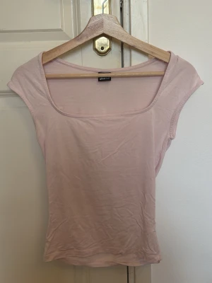 Ljusrosa topp med bred ringning - Säljer en ljusrosa topp med bred, fyrkantig ringning och korta ärmar. Toppen har en enkel och stilren design som passar perfekt till jeans eller kjol. Materialet känns mjukt och bekvämt mot huden.