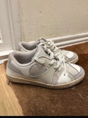 Vita sneakers från AIRWALK X Han Kjøbenhavn - Snygga vita sneakers från Han Kjøbenhavn med grå och beige detaljer. Skorna har en låg siluett, rund tå och snörning framtill. Ovandelen är i en mix av läder och mesh för en sportig look. Perfekta för dig som gillar stilrena och trendiga sneakers.