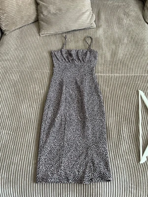 Svart blommig midiklänning med smala band - Snygg svart klänning med små vita blommor och smala axelband. Klänningen har en figurnära passform och slutar strax under knäet. Perfekt för sommaren med sitt lätta material och feminina look.