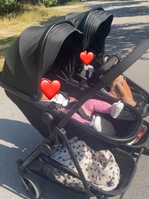 Svart syskonvagn med stora hjul - Säljer en svart syskonvagn med två sittdelar bredvid varandra. Vagnen har stora hjul, justerbart handtag och rymlig varukorg undertill. Perfekt för två barn och smidig att köra både i stan och på promenader. Det är en och samma justerbara del som används för både sitt och ligg läge, anpassad för både äldre barn och mindre bebisar