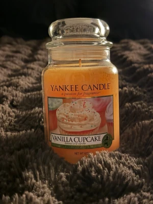 Yankee Candle Vanilla Cupcake ljus - Doftljus i glasburk från Yankee Candle med doften Vanilla Cupcake. Ljusets färg är ljusgul och burken har ett klassiskt lock. Perfekt för att skapa mysig stämning hemma med en söt och bakverksinspirerad doft.