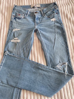 2000s hollister lågmidjade jeans - jättesnygga och eftertraktade ljusblåa jeans från Hollister med slitningar, strl W25(~XS), L33 //  -midja 36cm tvärsöver -innerbenslängd 82cm -benöppning 20,5cm -grenhöjd 16,5cm -lår 26cm