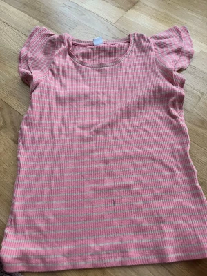 Rosa och beige randig topp Lindex - Söt topp från Lindex i storlek 170 med rosa och beige smala ränder. Toppen har korta puffärmar och är ribbad i materialet vilket ger en skön stretchig känsla. Perfekt för dig som gillar en enkel men ändå söt stil.