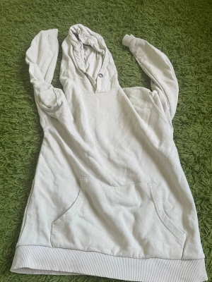 Vit hoodie med magficka och huva - Säljer en enkel vit hoodie med stor magficka och huva. Hoodien har ribbade muddar nedtill och vid ärmsluten samt en knappdetalj vid halsen. Perfekt för chill dagar och passar till det mesta. Materialet känns mjukt och bekvämt.