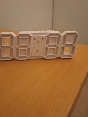 Digital väggklocka i vit plast - Säljer en modern digital väggklocka i vit plast med stora LED-inspirerade siffror. Klockan har knappar på ovansidan för inställningar och kan drivas med batteri eller strömadapter. Perfekt för att hålla koll på tiden i sovrummet eller kontoret.