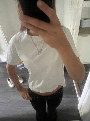 Vit  t-shirt - Säljer en enkel vit t-shirt med korta ärmar och rund hals. Perfekt till jeans eller kjol för en clean och avslappnad look. Materialet känns mjukt och skönt mot huden.