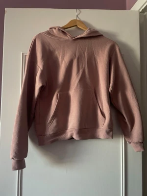 Rosa hoodie  - En enkel och snygg ljusrosa hoodie med huva och stor magficka framtill. Hoodien har ribbade muddar vid ärmslut och nederkant. Perfekt för en avslappnad och chill stil. Materialet känns mjukt och bekvämt.