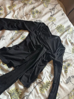 Svart omlottopp med långa ärmar - Snygg svart omlottopp med långa ärmar och knytband i midjan. Perfekt för dig som gillar en stilren och enkel look. Tunnare material som känns skönt mot huden och passar till många olika outfits.