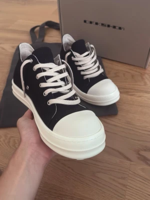 Rick Owen’s Ramones low canvas - säljer ett par klassiska Rick Owens DRKSHDW Ramones Low i svart canvas. Ikonisk silhuett med den kraftiga vita gummisulan, den karakteristiska tåhättan och kraftiga vita snören med metallöljetter. Skorna kommer med tillhörande kartong och skopåse (dustbag). Skicket är helt nytt och anledningen till att jag säljer dem är att de inte passar mig.