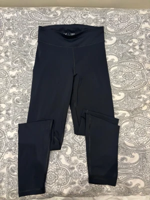 Svarta höga leggings med stretch - Snygga svarta leggings med hög midja och stretchigt material som sitter skönt på kroppen. Perfekta för träning eller chill. De har en enkel design utan synliga loggor framtill och är helsvarta. Materialet känns mjukt och följsamt.