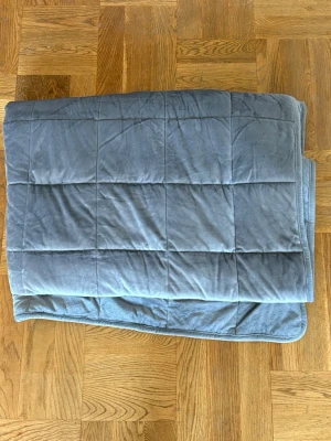Grå tyngtäcke i rutigt mönster 6kg - Mysig grå tyngdfilt med rutigt mönster. Filten är tillverkad i mjukt tyg och har en kvadratisk quiltad design. 