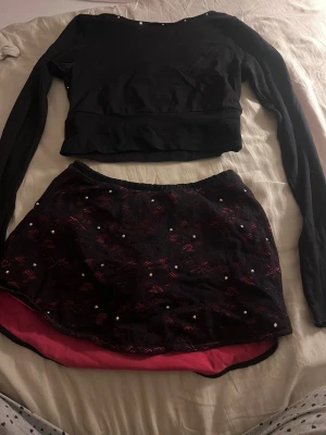 Karisma sätt i svart, rosa  - Säljer en svart croppad topp med rosa detaljer med långa ärmar den sitter lite som en magtröja men brukar ha ett linne under med en matchade kjol från karisma knappt använda väldigt fint 