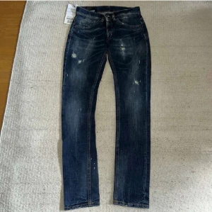 Dondup mörkblå jeans  - Säljer ett par mörkblå Dondup jeans med slitningar och lätt tvättade detaljer. Jeansen har rak passform och klassisk femficksdesign. Snygga detaljer med slitna partier och lite färgstänk för en trendig look. Perfekta för dig som gillar en avslappnad stil.