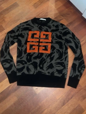 Svart och grå stickad tröja Givenchy - Snygg stickad tröja från Givenchy i svart och grått med ett stort orange broderat mönster på bröstet. Xs men passar s också den är i perfekt skick och säljer den eftersom den är liten på mig 