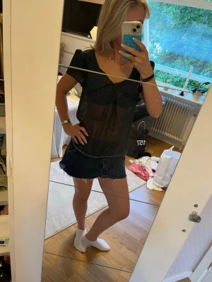 Svart mesh topp med små prickar - Säljer en svart mesh topp med små vita prickar och v-ringad hals. Toppen är kortärmad och har en lätt transparent look som ger en trendig vibe. Perfekt att styla med jeans eller kjol för en cool outfit. Omsydd.