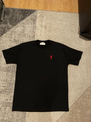 Svart t-shirt  - Snygg svart t-shirt med en liten röd hjärtdetalj broderad på bröstet. Klassisk passform och rund halsringning. Perfekt till jeans eller shorts för en clean och stilren look.
