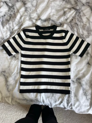 Randig svartvit t-shirt - Säljer en stilren svartvit randig t-shirt med korta ärmar och rund hals. T-shirten har breda horisontella ränder och är gjord i ett mjukt bomullsmaterial som känns skönt mot huden. Perfekt för en avslappnad look.