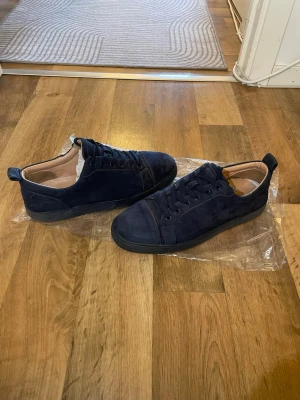 Mörkblå mocka sneakers från Christian Louboutin  - Snygga mörkblå sneakers i mocka med klassisk låg profil och svarta snören. Skorna har en stilren design med diskreta sömmar och svart sula. Perfekta för dig som gillar en clean och modern look. Storlek 44 passar 43 obs skorna har lagats lite grann 