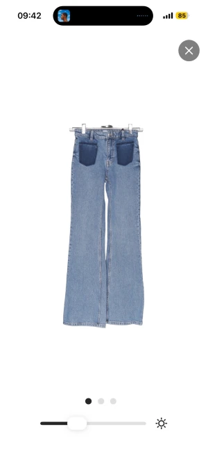 Ljusblå utsvängda jeans med kontrastfickor - Säljer ett par ljusblå jeans med utsvängda ben och höga midja. Framtill finns två mörkblå kontrastfickor som ger en cool retrovibe. Klassisk femficksmodell baktill. Perfekta för dig som gillar en unik och trendig look.