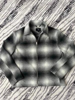 Grå overshirt med rutigt mönster - Snygg overshirt från H&M i grått och svart rutigt mönster. Jackan har dragkedja framtill, klassisk krage och raka ärmar. Materialet är mjukt och borstat, perfekt för lager på lager. Enkel och stilren design som passar till det mesta.  Lite för står för mig därför säljer jag. De är riktigt fint och passar med allt. Går alltid att diskutera.