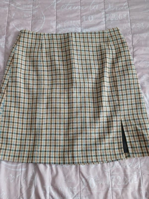 Beige rutig kjol med slits - Säljer en beige kjol med rutigt mönster i svart, blått och brunt. Kjolen har en rak passform och en liten slits framtill. Materialet känns mjukt och har en klassisk look som passar till många olika stilar.