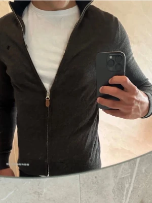 Mörkgrå ziptröja i merinoull Morris - Snygg mörkbrun ziptröja från Morris i 100% merinoull. Tröjan har fulzip och en stilren, smal passform. Perfekt att bära över en t-shirt för en clean och modern look. Vid frågor är det bara att skicka ett meddelande😃 skick är 9.5/10 använde max 6 gånger säljer pga att den inte passar längre. Storlek är xs men passar bättre S