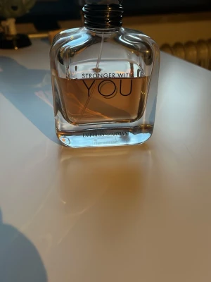 Stronger With You parfym - Stronger With You från Emporio Armani är en elegant parfym i en genomskinlig, fyrkantig glasflaska med rundade kanter. Doften har en varm bärnstensfärgad vätska och flaskan har svart spraykork. Perfekt för dig som gillar stilrena och moderna dofter. 100ml flaska ca 3/4 full