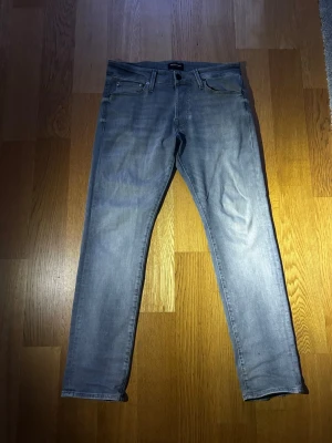 Ljusgrå Jack and Jones jeans - Säljer ett par ljusgrå slim fit jeans med klassisk femficksdesign och dragkedjegylf. Jeansen har raka ben och subtila slitningar för en avslappnad look. Perfekta till en casual outfit och passar till det mesta i garderoben.