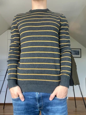 Randig tröja grå och gul - Gul och grå randig tröja från Angelo Litrico tillverkad i 100% bomull. Strl S. Inga defekter. Modellen är 178 cm och väger 77 kg. Hör gärna av dig vid frågor!