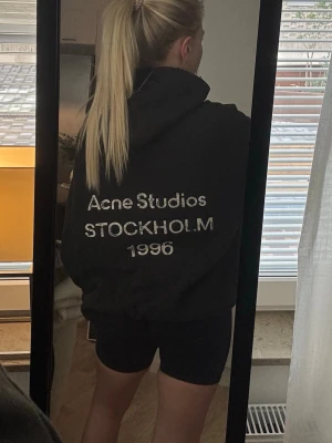 Svart hoodie Acne Studios - Svart oversized hoodie från Acne Studios med tryck på ryggen där det står 'Acne Studios STOCKHOLM 1996'. Hoodien har huva och är gjord i mjukt material, perfekt för en chill och stilren look.