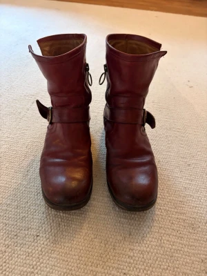 Vinröda Fiorentini+Baker boots  - Säljer ett par vinröda boots i läder med rund tå och  spänne i metall på sidan. Lite som en snygg MC kjänga. De är säkert 15 år gamla men samma modell säljs fortfarande, en klassiker. Köpte på Biblioteksgatan i Stockholm för nypris 3500kr Ksnske att man vill byta ut sulan bara.  