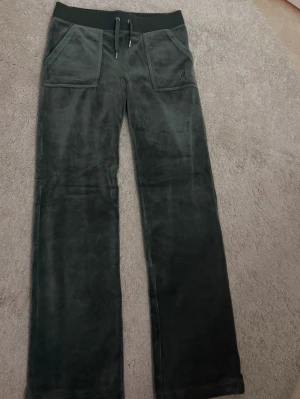 Mörkgröna  mjukisbyxor - Mörkgröna mjukisbyxor i mjuk velour med resår i midjan. Byxorna har raka ben, två stora fickor fram och en broderad JC-logga på ena fickan. Perfekta för chill dagar och riktigt sköna att ha på sig.
