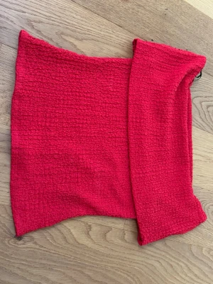 Röd bandeau tubtopp - Säljer en röd bandeau tubtopp i stretchigt, strukturerat tyg. Toppen är axelbandslös och har en smockad yta som ger en cool och trendig look. Perfekt att styla med höga jeans eller kjol för en snygg outfit.