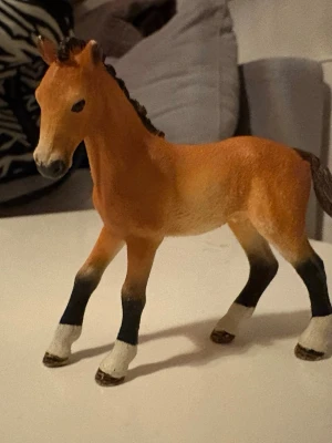 Schleich häst - Säljer en realistisk hästfigur i plast med brun kropp, svart man och svans samt vita och svarta detaljer på benen. Perfekt som dekoration eller leksak för dig som gillar djur och samlarfigurer.