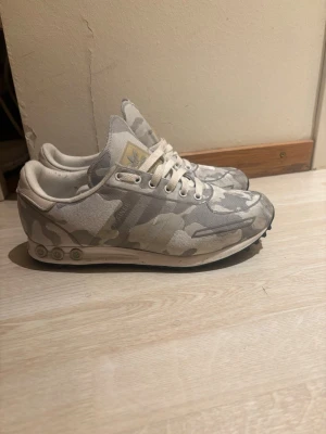 La trainers adidas - Säljer ett par Adidas sneakers med grått och vitt camomönster. Skorna har lågt skaft, vita snören och detaljer i mesh och textil. Klassisk Adidas-logga på plösen i guld. Snygga och unika sneakers för dig som vill sticka ut.