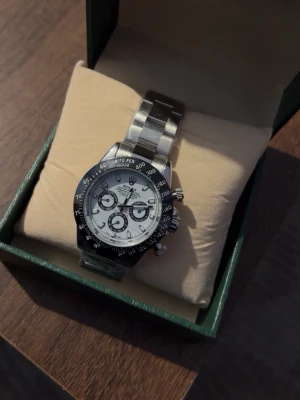 Klocka - Snygg kronografklocka i silver med vit urtavla och svart bezel. Klockan har tre mindre urtavlor, tydliga markeringar och robust länkarmband i metall. Perfekt accessoar för dig som gillar klassisk och sportig stil.